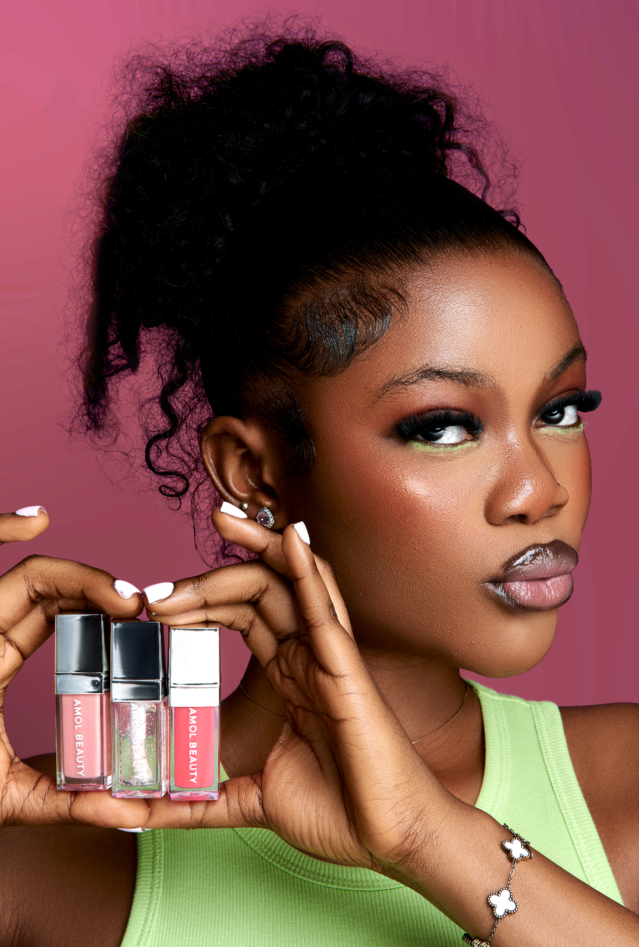 AMOL BEAUTY model holding three lip gloss shades